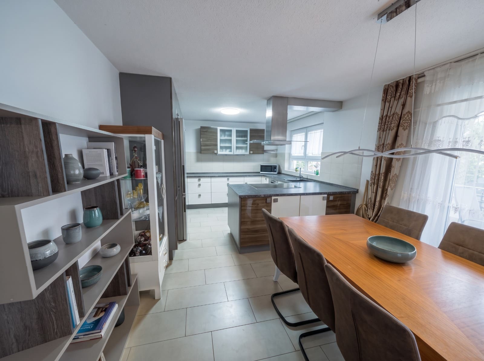 Moderne Einbauküche mit Kochinsel, Dunstabzug und angrenzendem Essbereich mit Holztisch