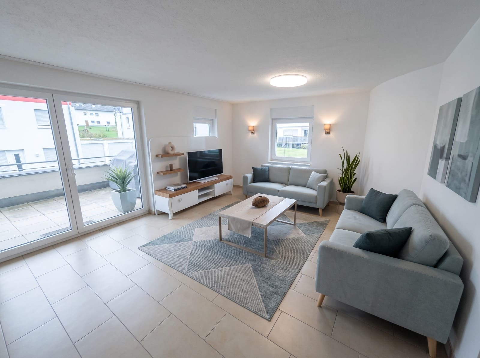 Helles Wohnzimmer mit zwei Sofas, Fliesenboden und bodentiefen Fenstern zur Terrasse